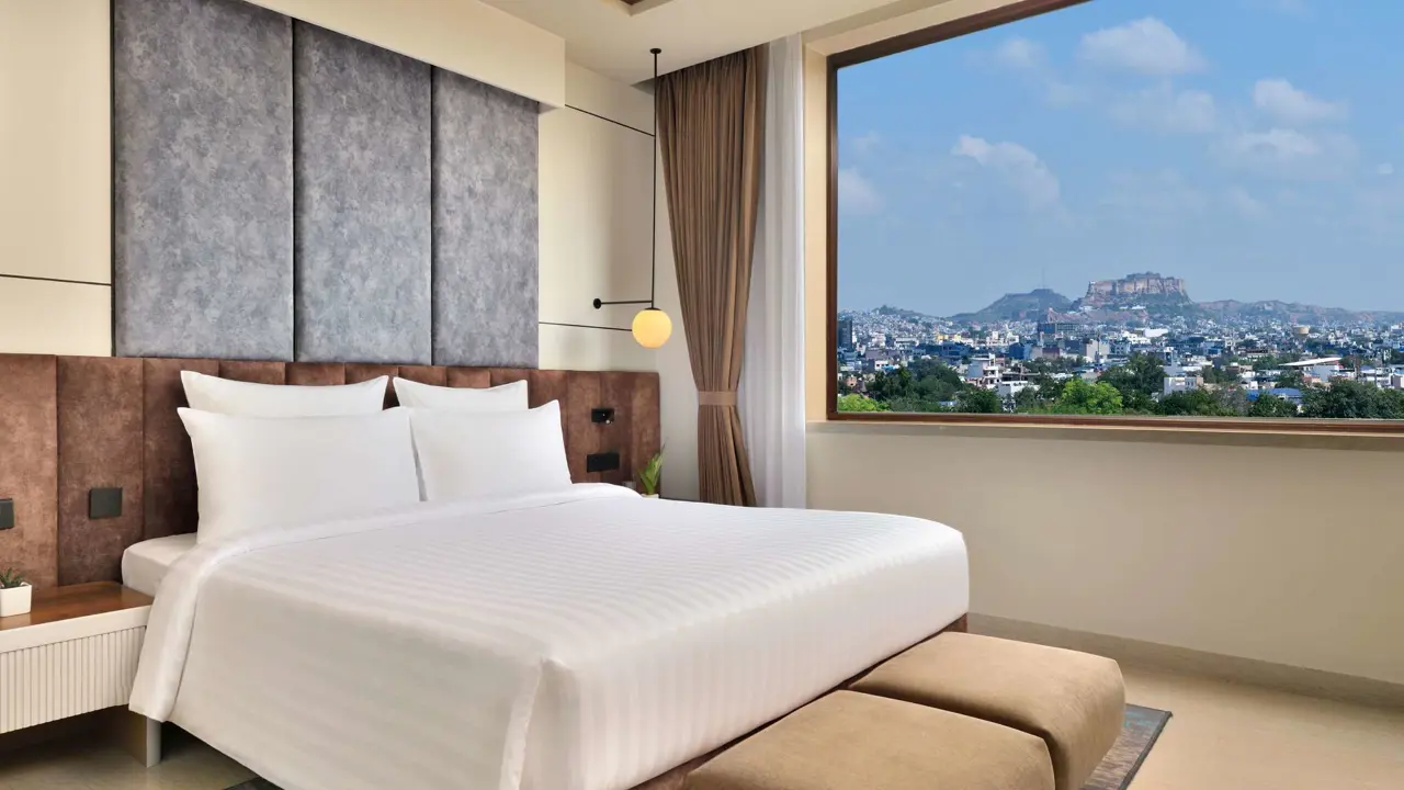 Bright guest room at Novotel Jodhpur with a king-size bed and large window offering city and fort views
