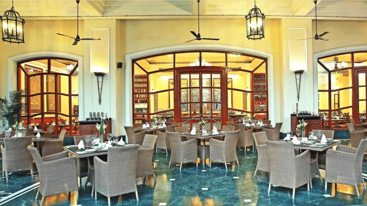 Elegant restaurant at Eros Hotel, New Delhi, with wicker chairs, set tables, and arched wooden windows
