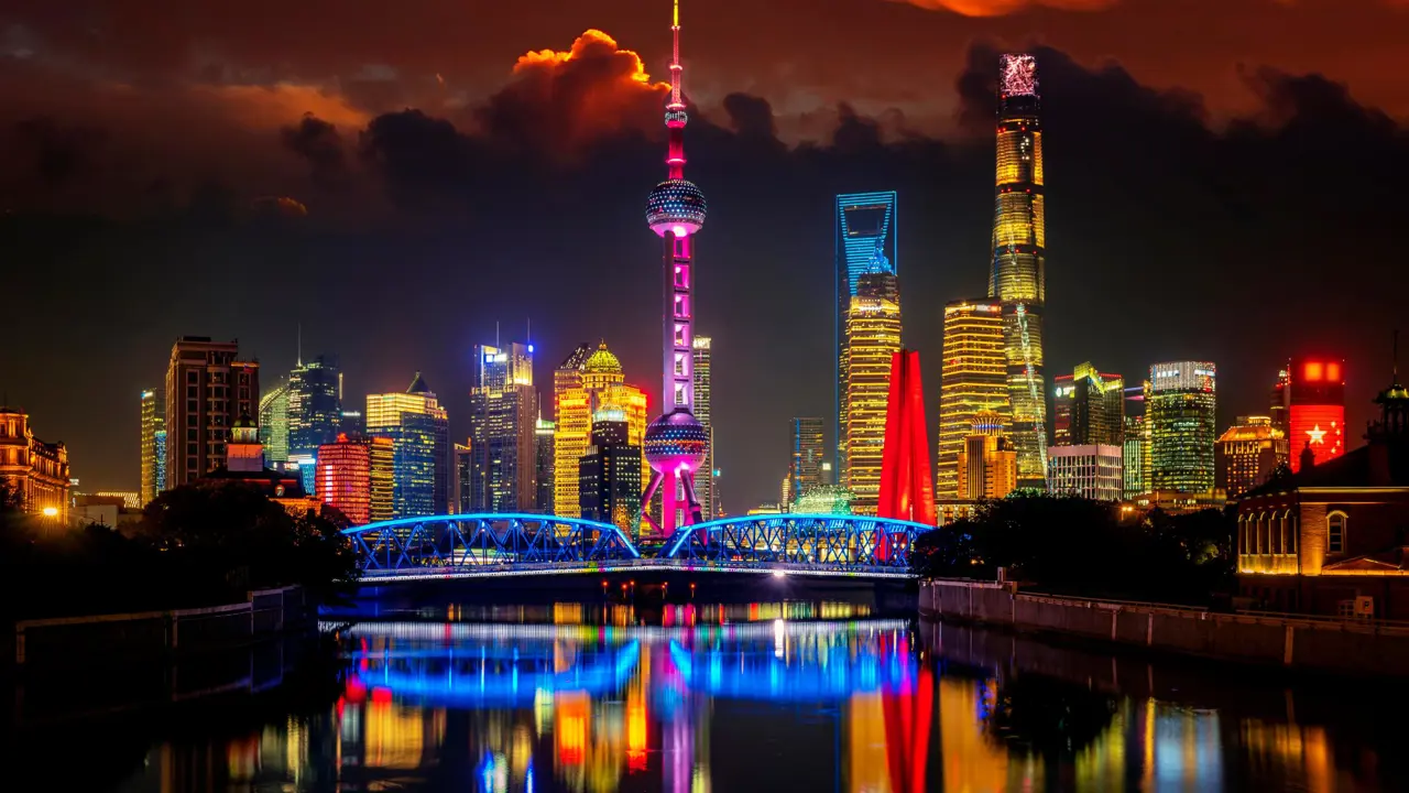 The Oriental Pearl Tower and modern skyscrapers lit in vibrant colours, reflected in the river at night in Shanghai, China