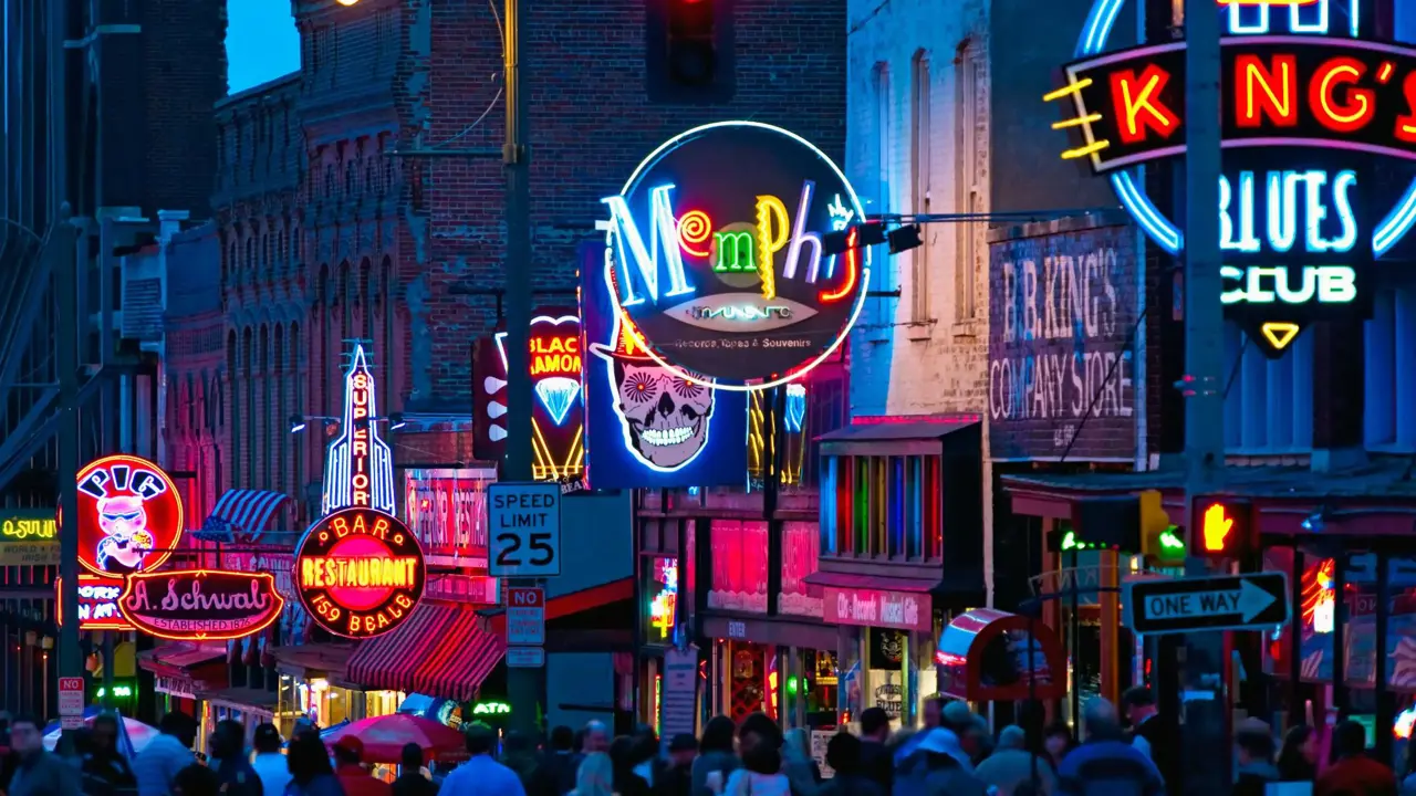Vibrant night scene of Beale Street in Memphis, Tennessee, with colourful neon signs for bars, restaurants, and blues clubs, and a crowd of people walking along the street