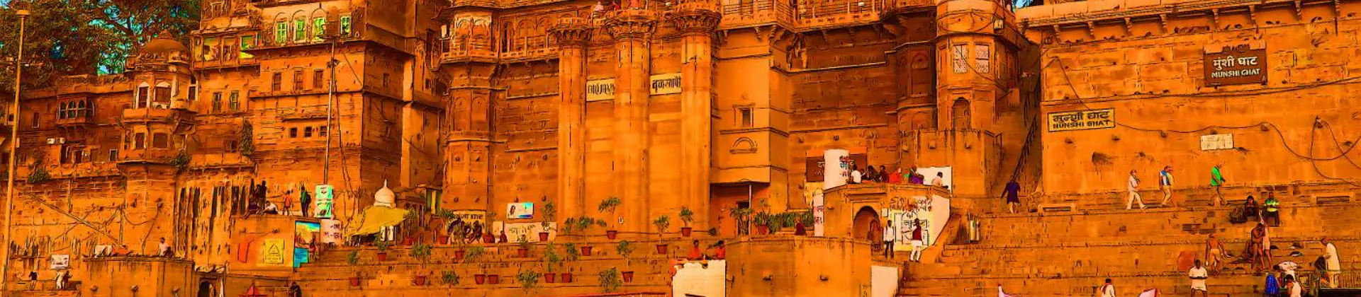 The ghats of Varanasi seen from the River Ganges, with historic sandstone palaces and colourful boats reflecting in the calm evening water