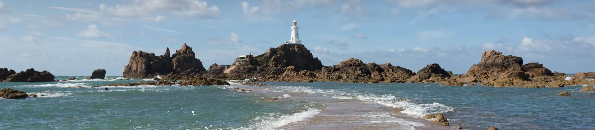 Long shot of the La Corbiere Causeway Light house, showing the sea below it, the rocks either side of it and a stone panel which runs towards it across the water