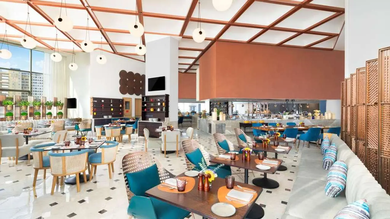 Spacious restaurant with colourful seating, a high ceiling and large windows at the Novotel New Delhi City Centre