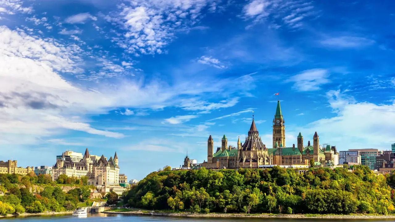 Ottawa skyline in Canada, showing Parliament Hill buildings above a river with trees in the foreground