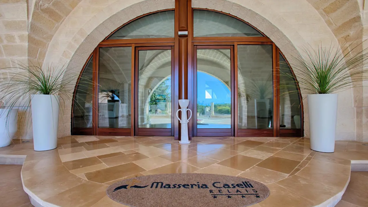 Entrance to Masseria Caselli Hotel, Italy, featuring arched stone architecture, large glass doors, and modern planters