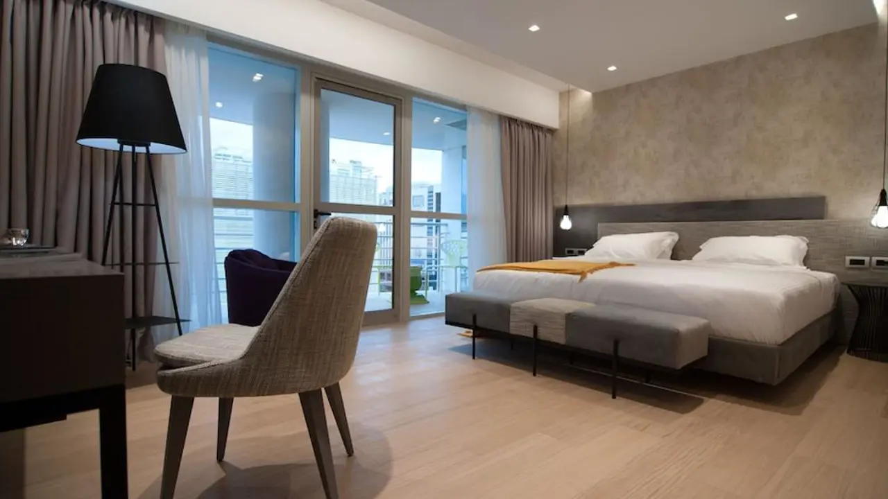 Modern hotel room at the Athenaeum Grand Hotel with a large bed, soft lighting, a desk, and city view balcony